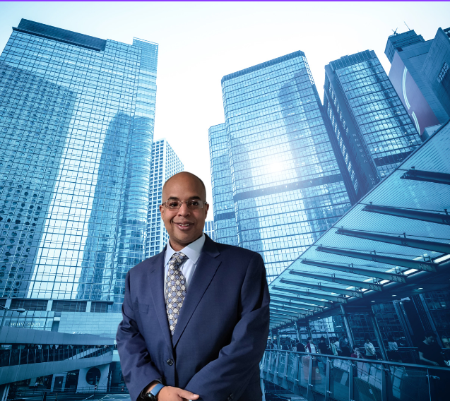 Anthony D. Riley standing in a navy suit against a city skyline