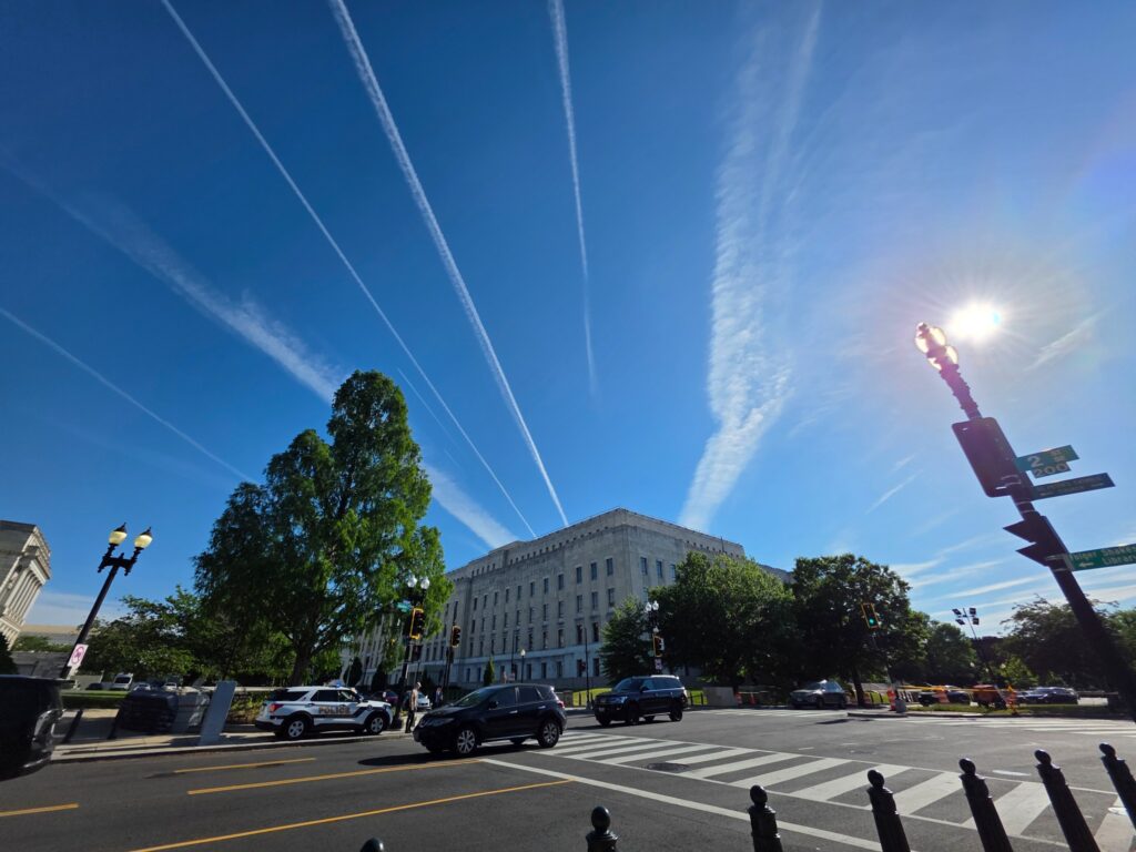 Washington DC street beneath bright blue sky and white aircraft trails