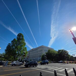 Washington DC street beneath bright blue sky and white aircraft trails